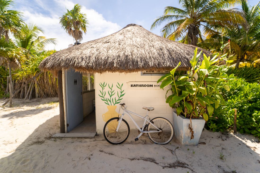 Palm-roofed bathroom hut and bicycle on the sand at Pronoia, Costa Maya
